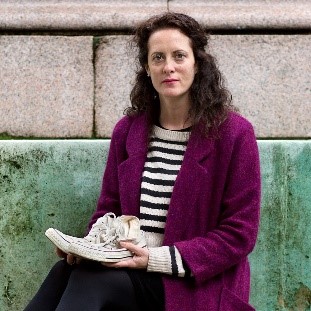 PICTURE OF ANNEMARIE COCKBURN FEMALE WITH DARK CURLY HAIR WEARING A STRIPEY BLACK AND WHITE SHIRT AND PURPLE CARDIGAN SITTING LOOKING AT CAMERA